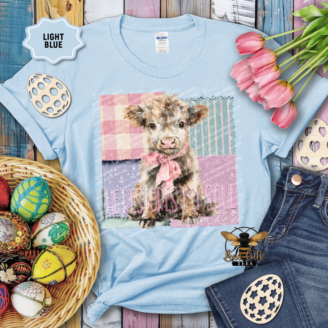 Light blue t-shirt with a cow print design on a wooden surface with Easter decorations.
