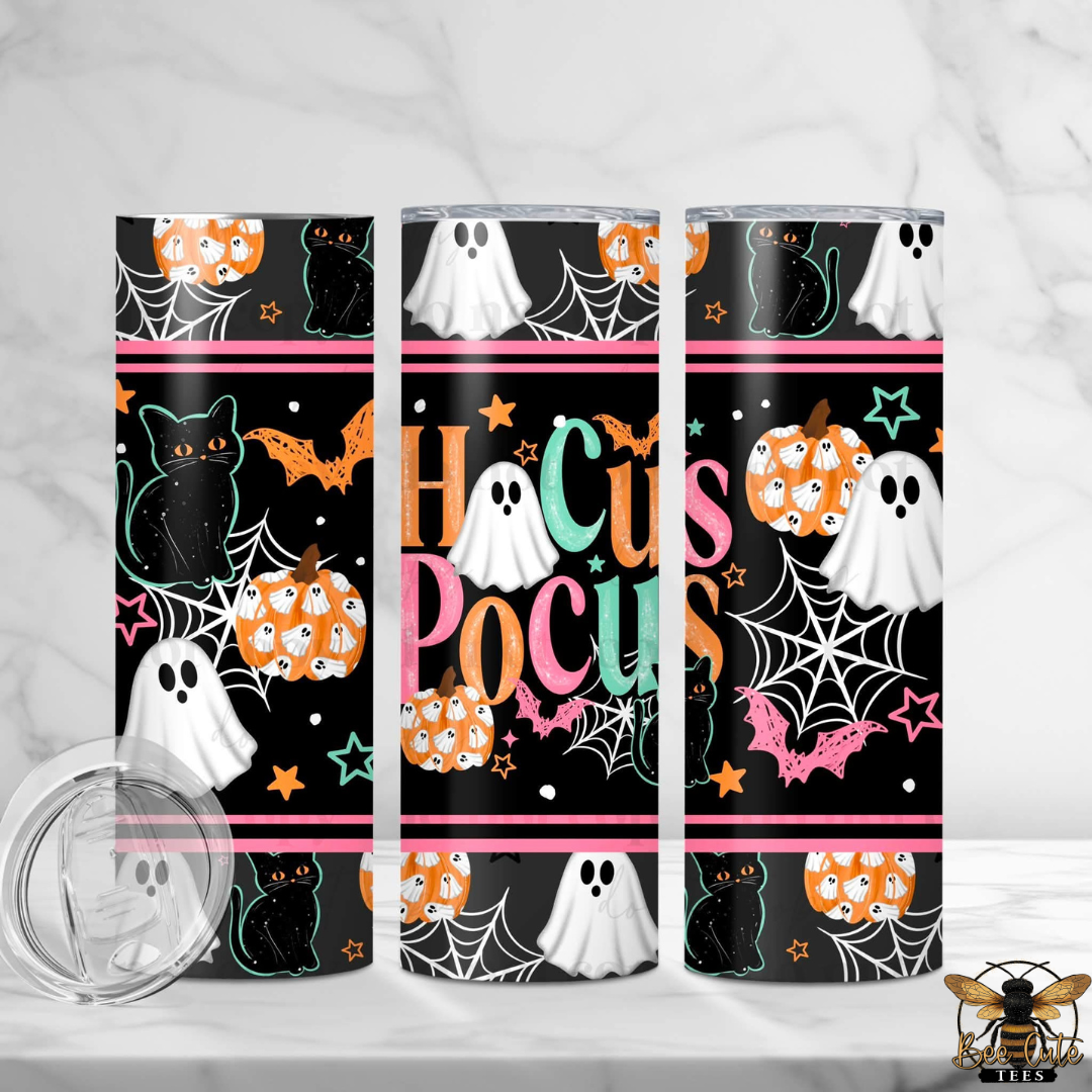 Three slim stainless steel tumblers with a Halloween-themed wrap design are displayed on a white marble surface. The design features a black background with orange pumpkins, white ghosts, black cats, pink bats, and the words 'HoCus Pocus' in colorful lettering.
