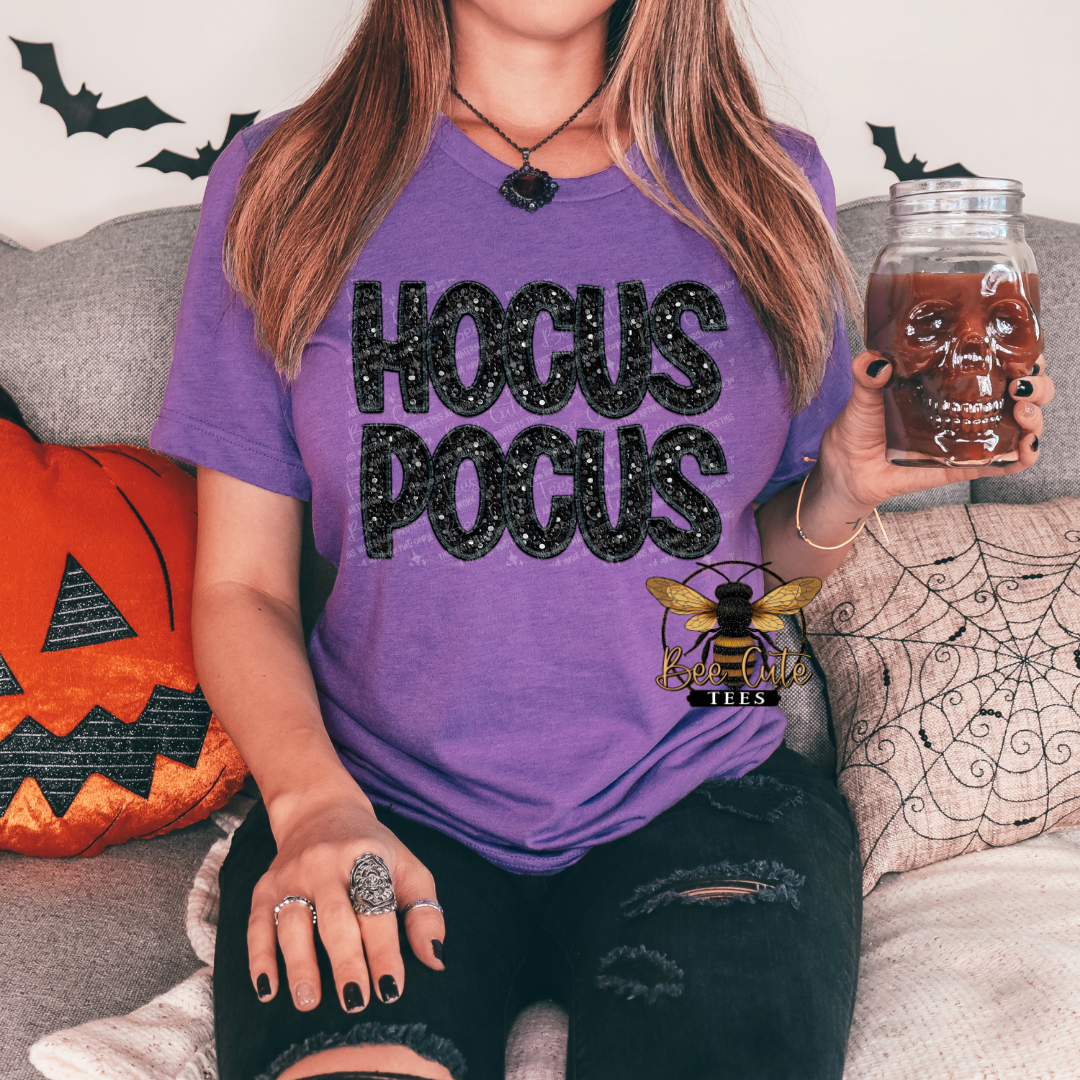 Person wearing a purple 'HOCUS POCUS' shirt with Halloween decorations in the background.