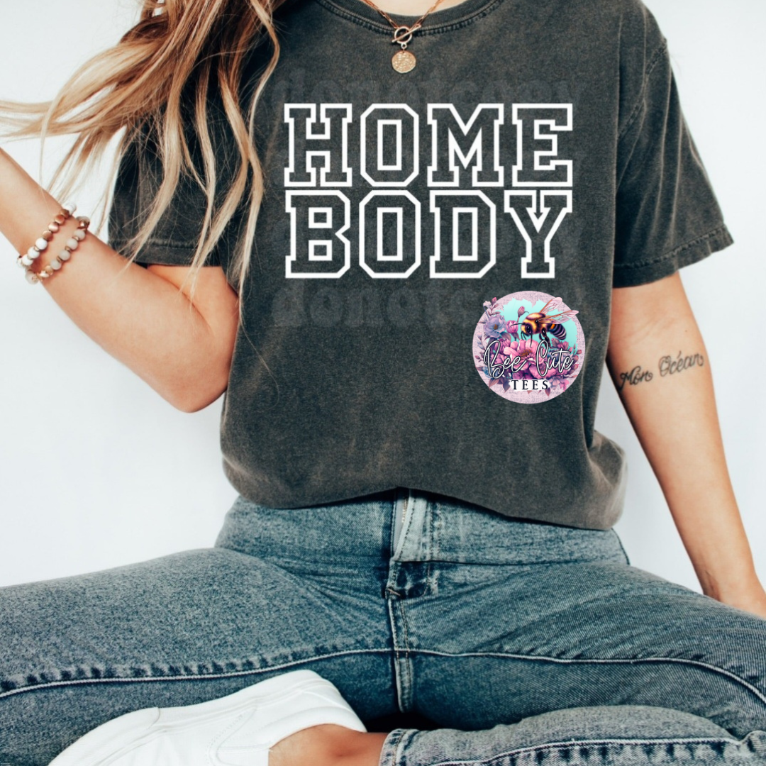Person wearing a 'HOME BODY' t-shirt with a colorful logo on a plain background