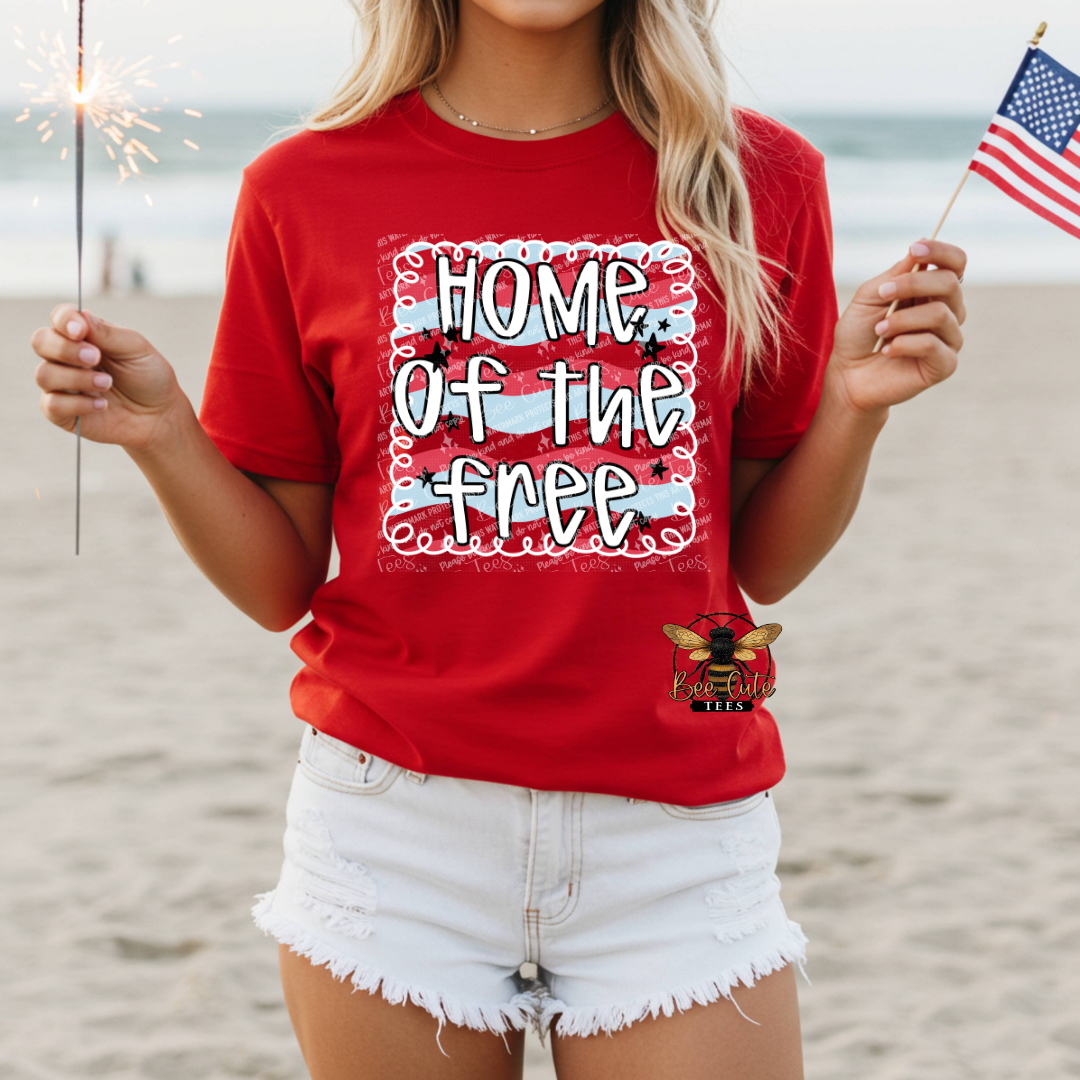 Person wearing a red 'Home of the Free' t-shirt on a beach with sparklers and an American flag.