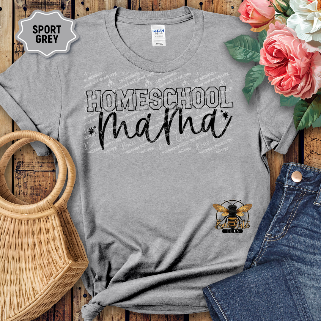 Gray t-shirt with 'Homeschool Mama' text and a logo, displayed with flowers and jeans on a wooden surface.