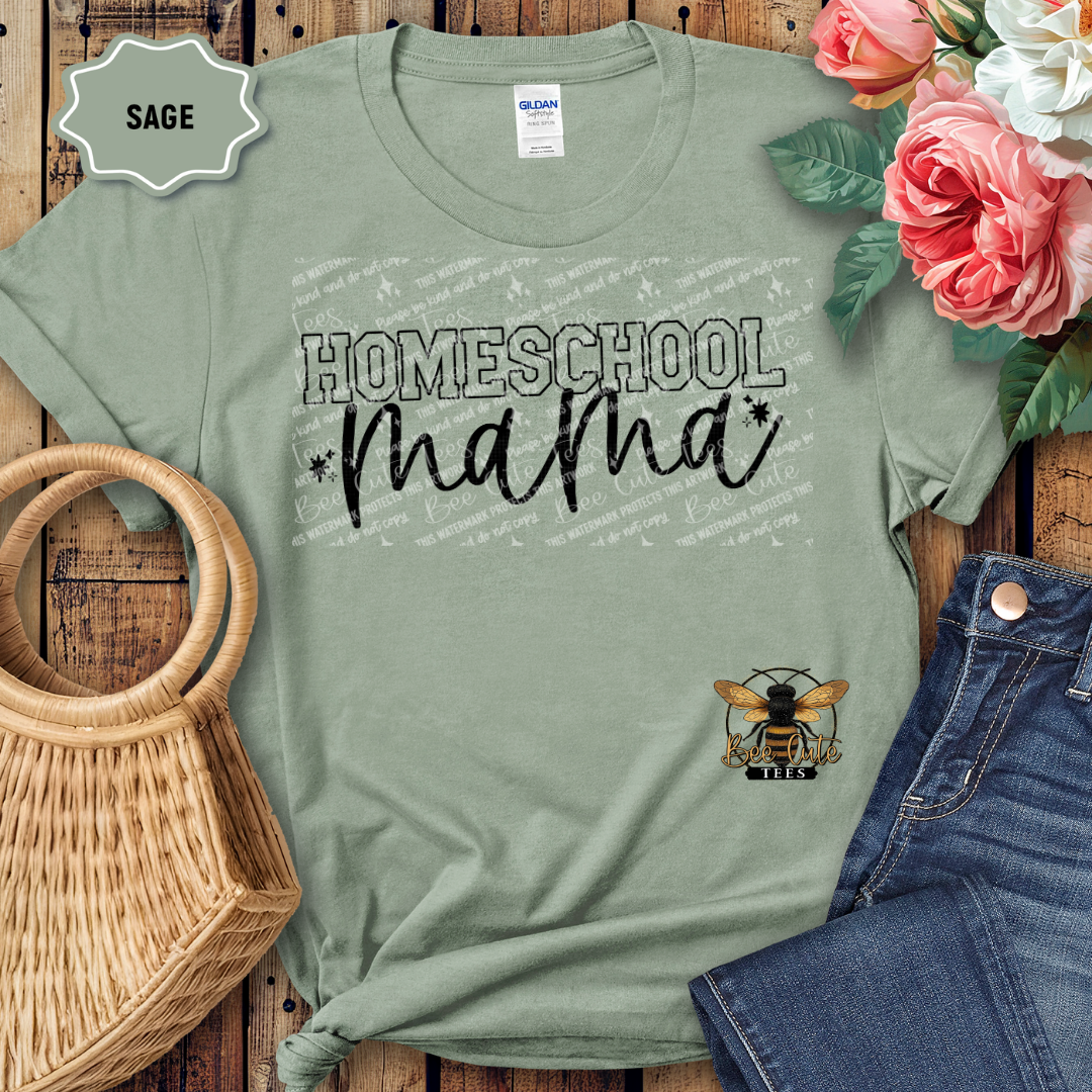 Sage green t-shirt with 'Homeschool Mama' text and bee logo on a wooden surface with flowers and jeans.