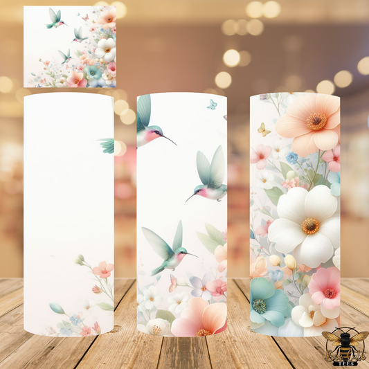 Three cylindrical candles with floral and hummingbird designs on a wooden surface.