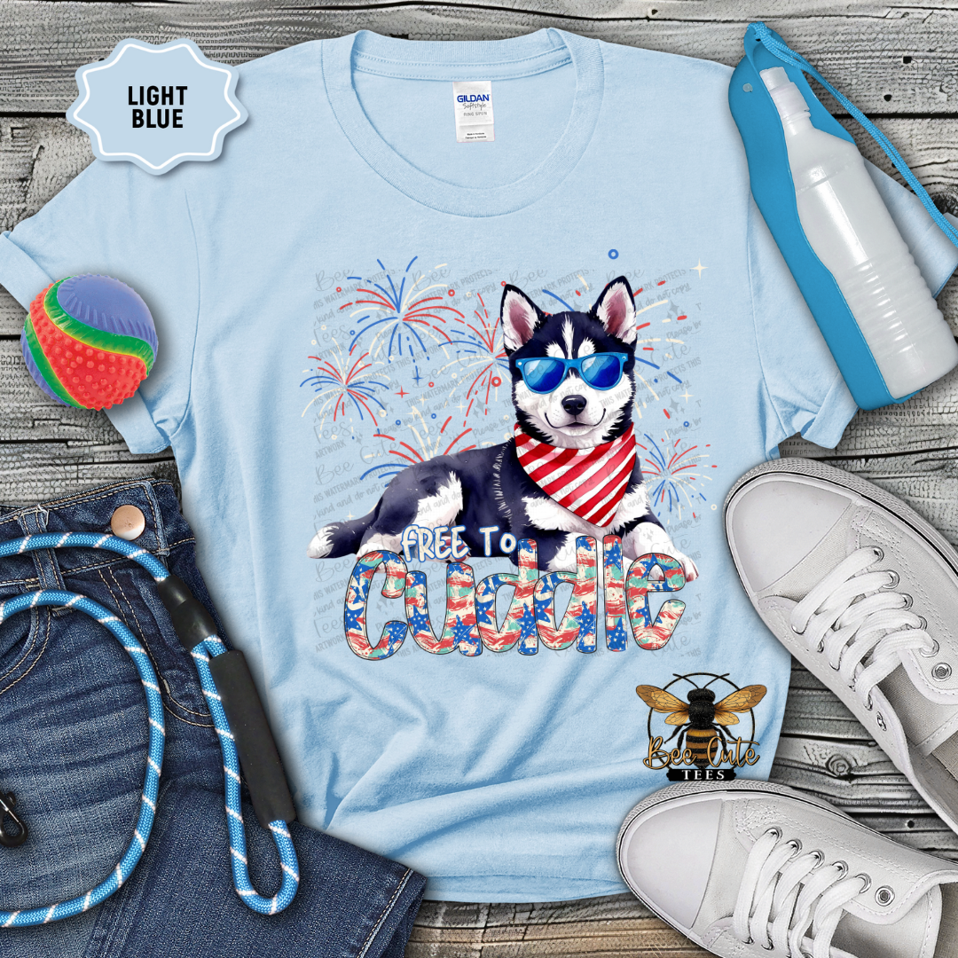 Light blue t-shirt with a dog graphic and 'Free to Cuddle' text, surrounded by accessories on a wooden surface.