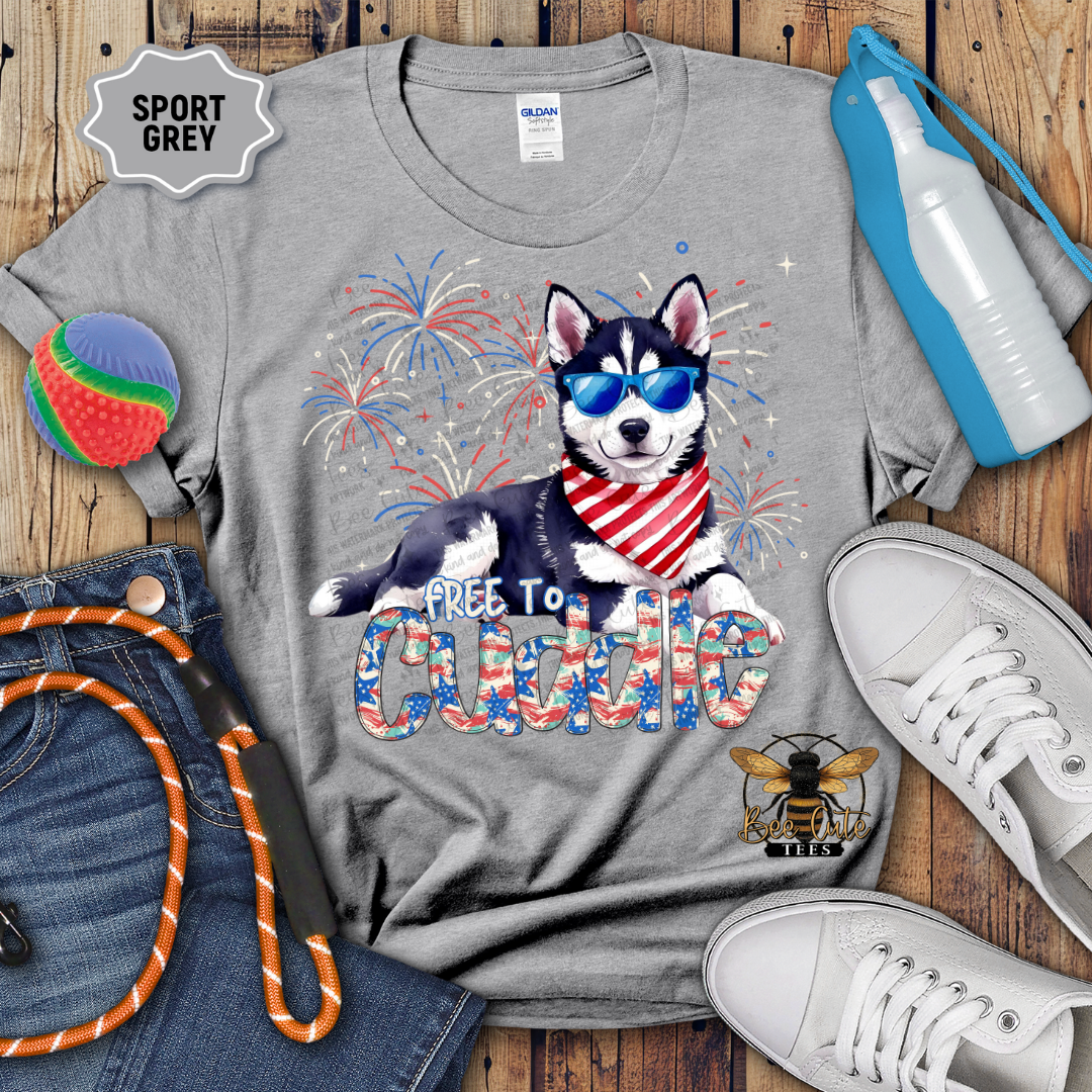 Gray t-shirt with a dog graphic and 'Free to cuddle' text on a wooden surface with accessories.