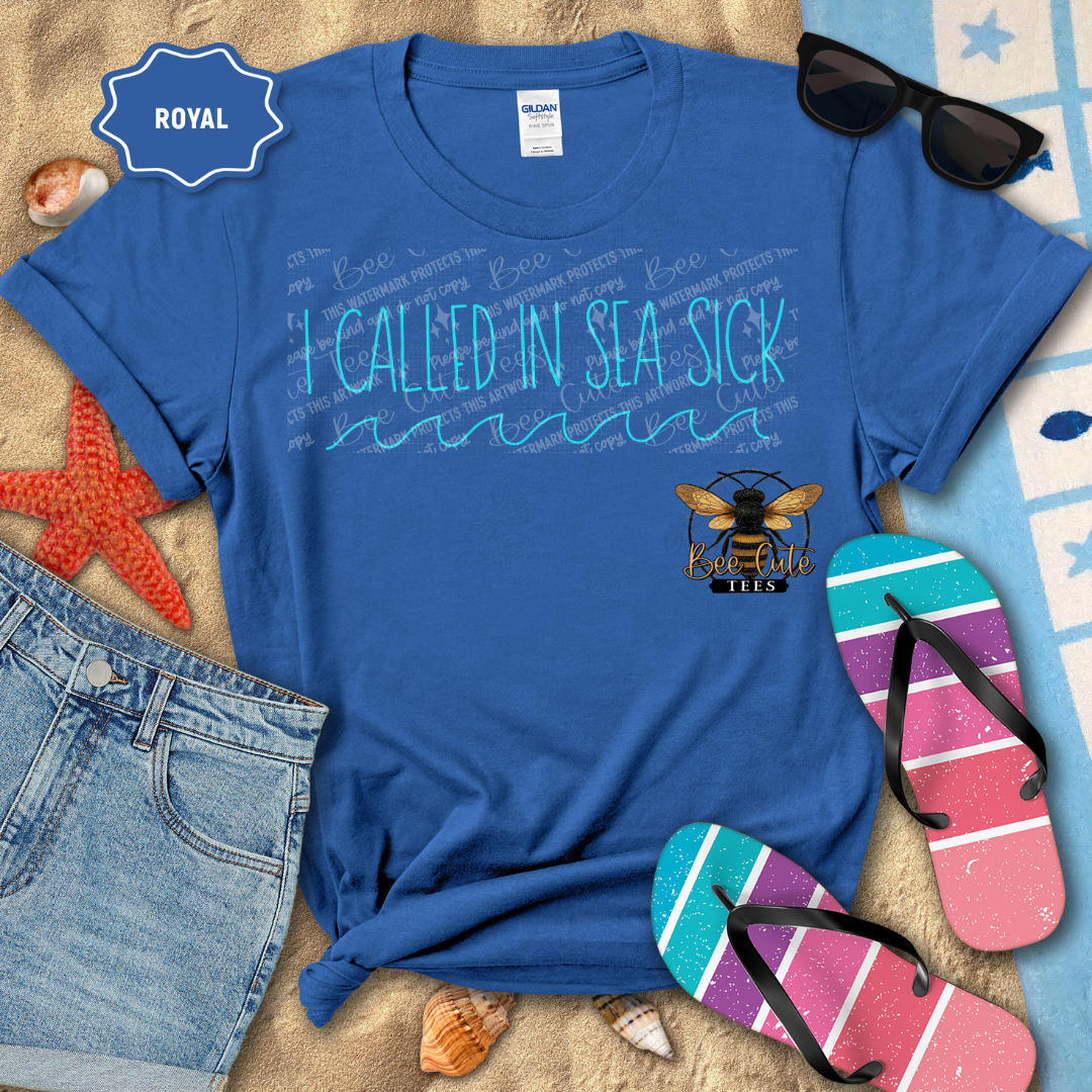 Blue t-shirt with 'I Called In Sea Sick' text and bee logo, surrounded by beach accessories.