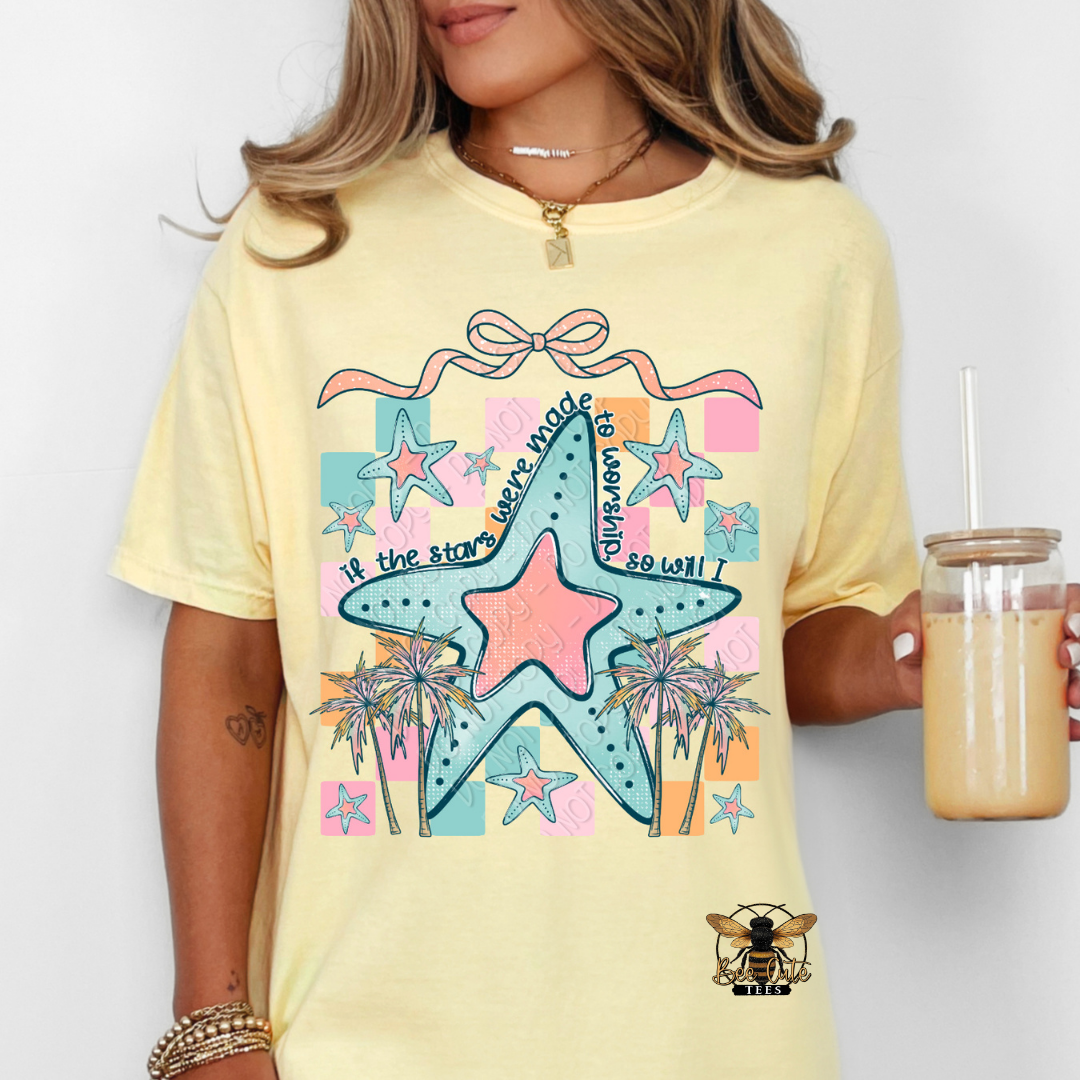 Person wearing a yellow t-shirt with a colorful star design, holding a drink.