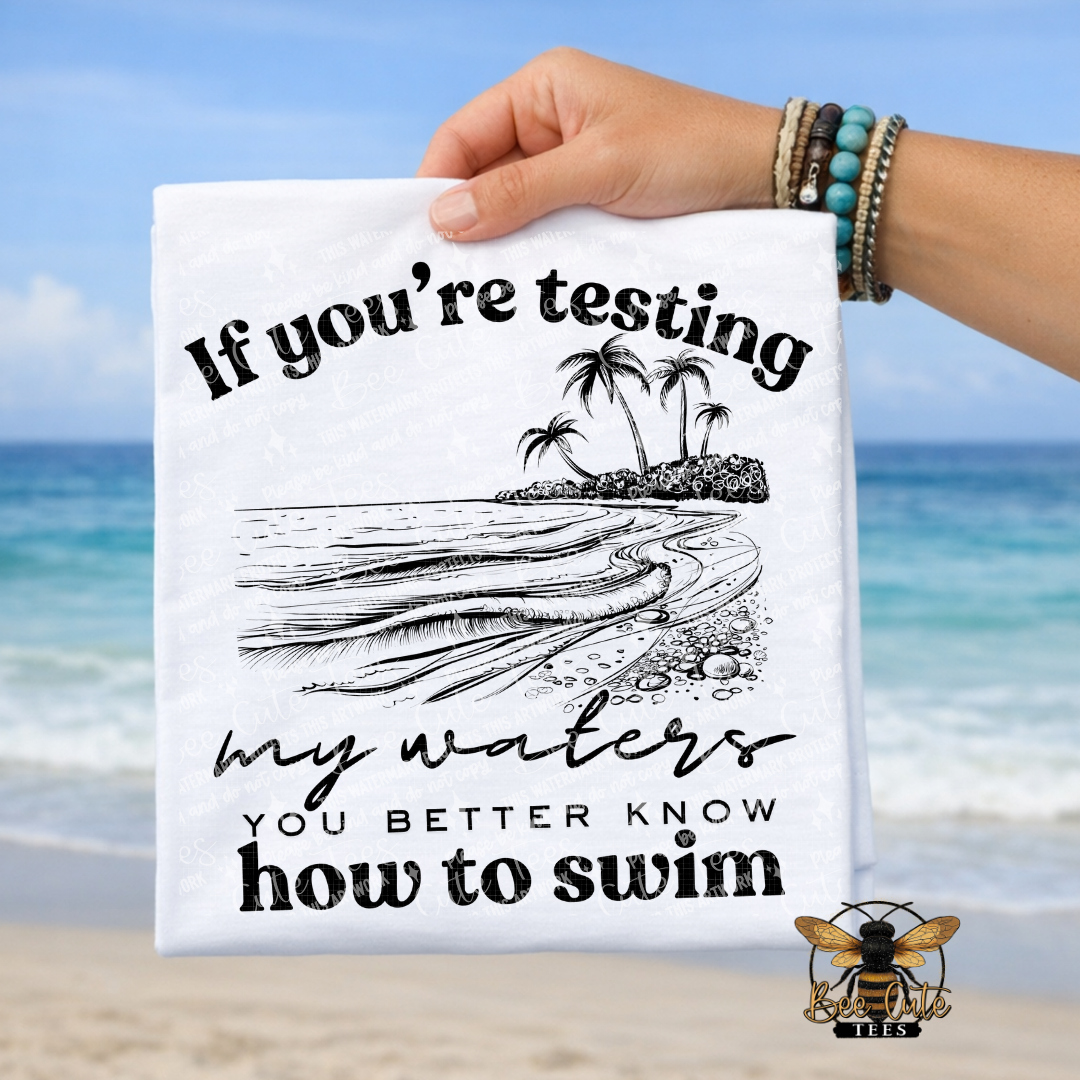 Hand holding a t-shirt with a beach design and text against a beach background