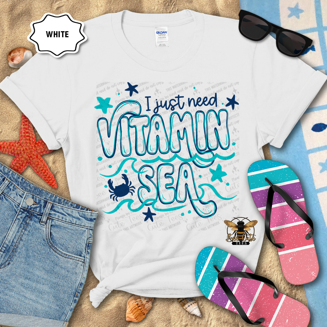 White t-shirt with 'I just need Vitamin Sea' design, sunglasses, denim shorts, and flip-flops on a beach-themed background.
