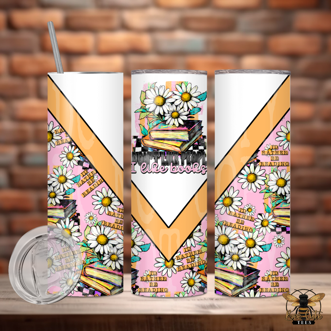 Three tumblers with book-themed designs on a wooden surface against a brick wall background.