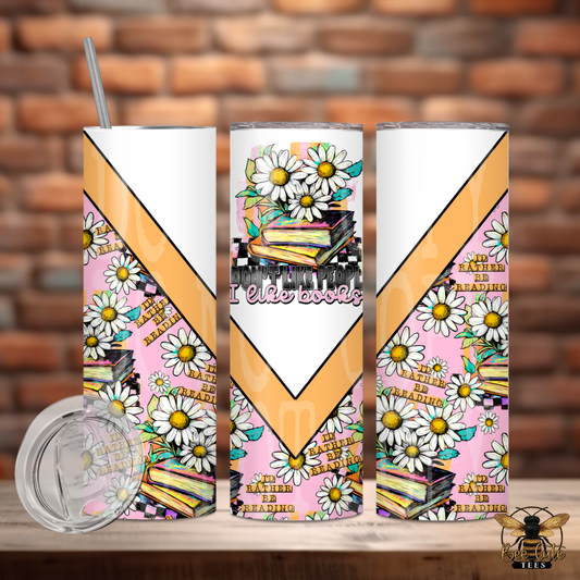 Three tumblers with book-themed designs on a wooden surface against a brick wall background.