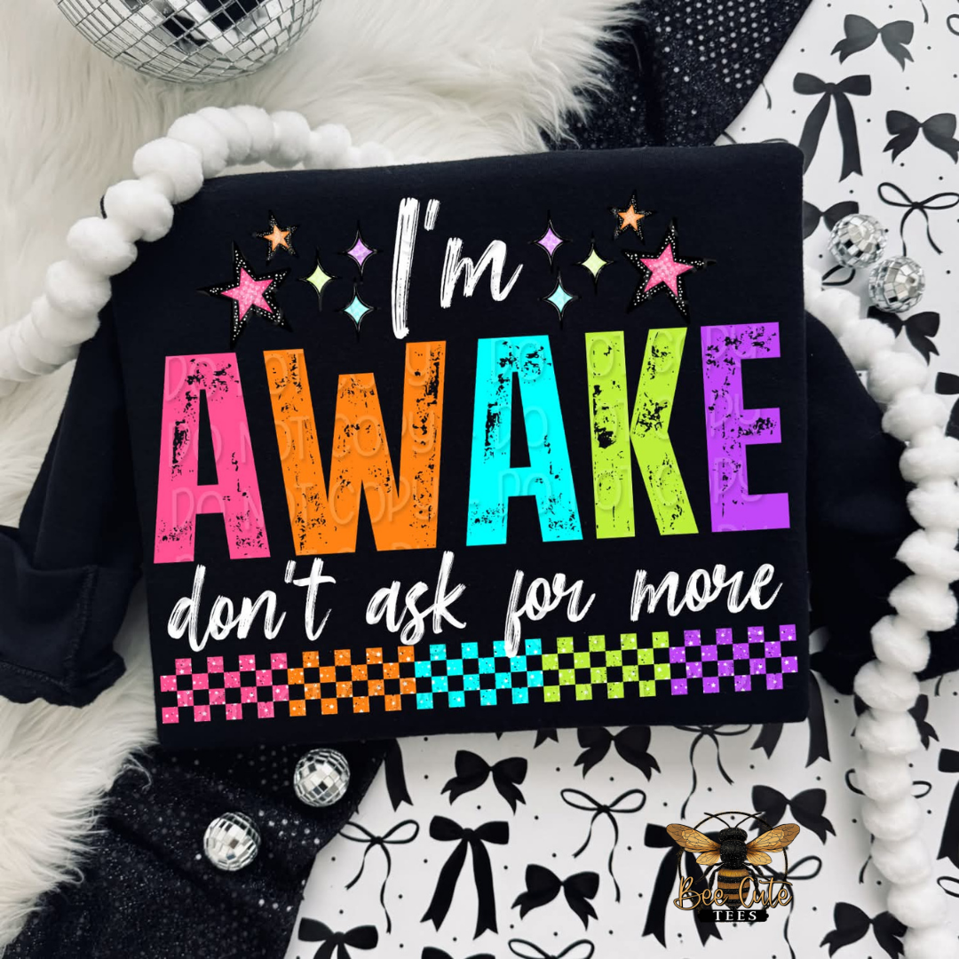 Black shirt with colorful text 'I'm AWAKE don't ask for more' on a patterned background.