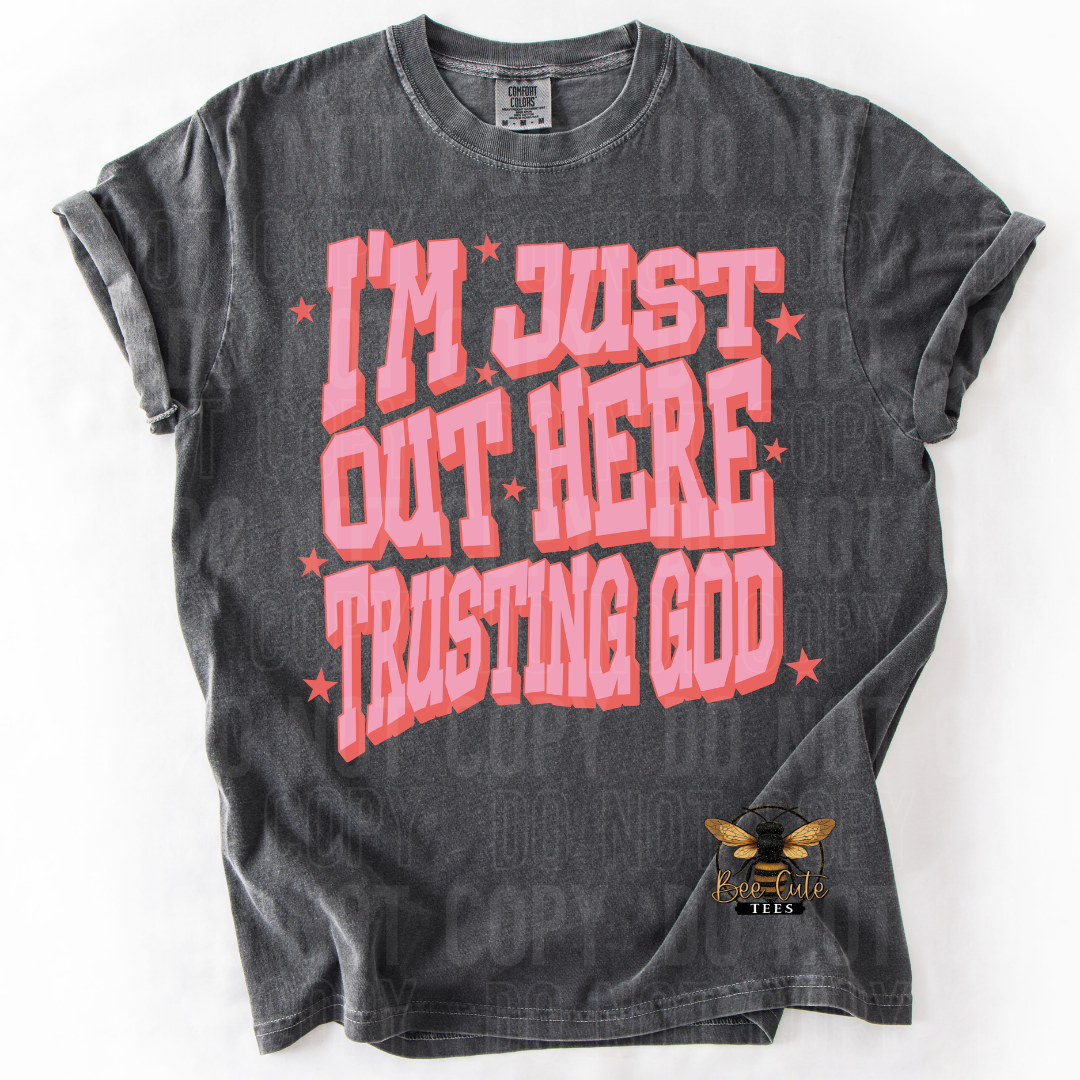 Black t-shirt with pink text 'I'm just out here trusting God' on a white background