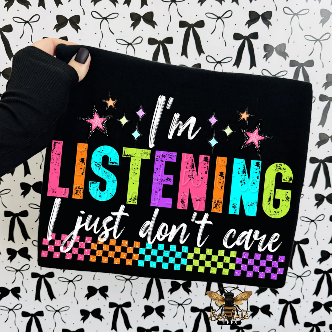 Black shirt with colorful text 'I'm Listening just don't care' held by a hand on a patterned background.