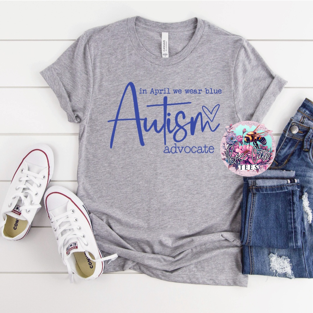 Gray t-shirt with 'Autism advocate' text, white sneakers, and jeans on a light wooden surface.