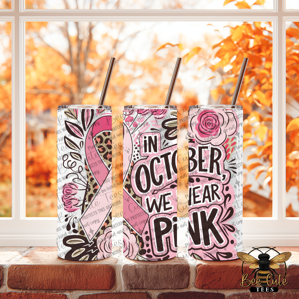 Three skinny tumblers with metal straws displayed on a brick windowsill, featuring pink and black autumn-themed designs including a pink ribbon, leopard print, and the text 'In October We Wear Pink'.