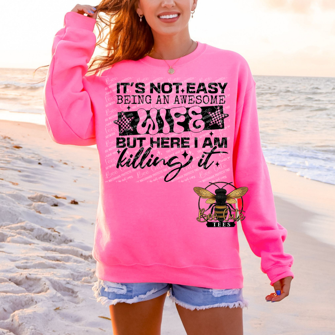 Person wearing a pink sweatshirt with text and a bee graphic on a beach.