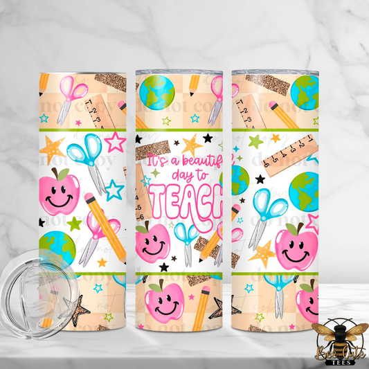 Three views of a 20 oz skinny tumbler with a school-themed print, including pink apples, scissors, pencils, stars, and the text 'It's a beautiful day to TEACH'. A clear lid is shown in the bottom left on a white marble background.