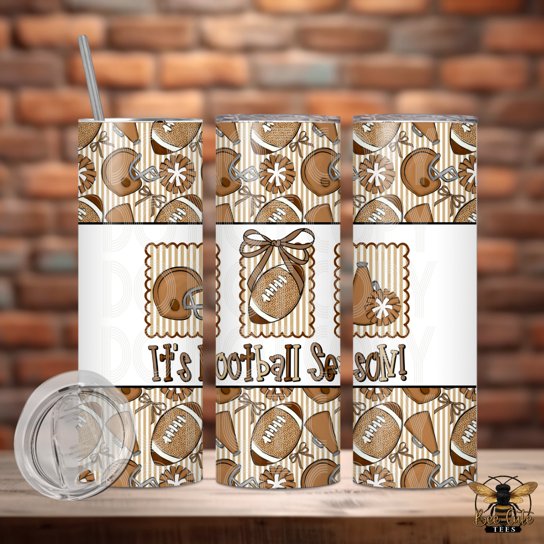 Three views of a stainless steel tumbler with a brown and beige football pattern, featuring the text 'It's Football Season!' on the front, shown on a wooden surface with a brick wall background. A clear lid is displayed in the lower left.