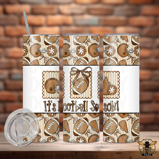 Three views of a stainless steel tumbler with a brown and beige football pattern, featuring the text 'It's Football Season!' on the front, shown on a wooden surface with a brick wall background. A clear lid is displayed in the lower left.