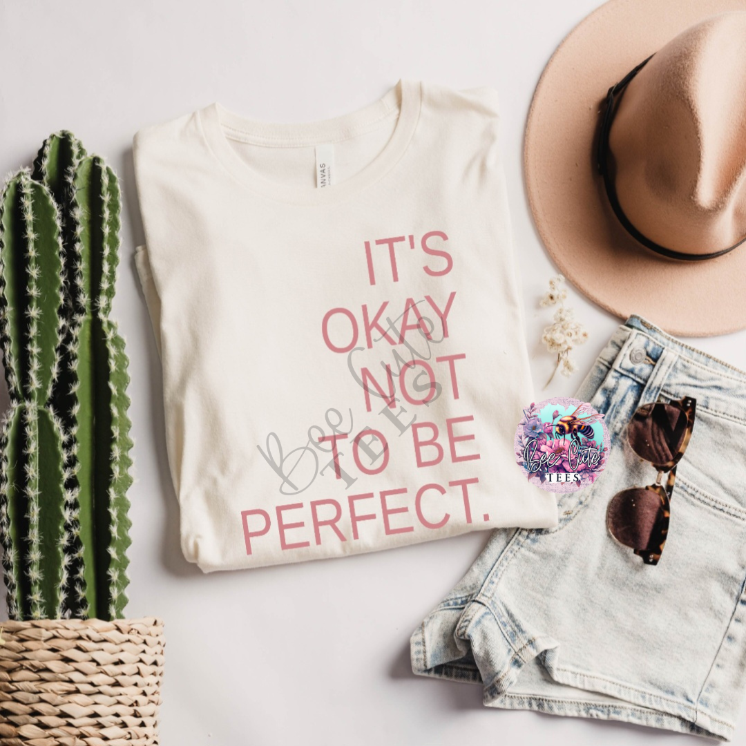 Beige sweatshirt with 'It's okay not to be perfect' text, hat, sunglasses, and cactus on a light surface