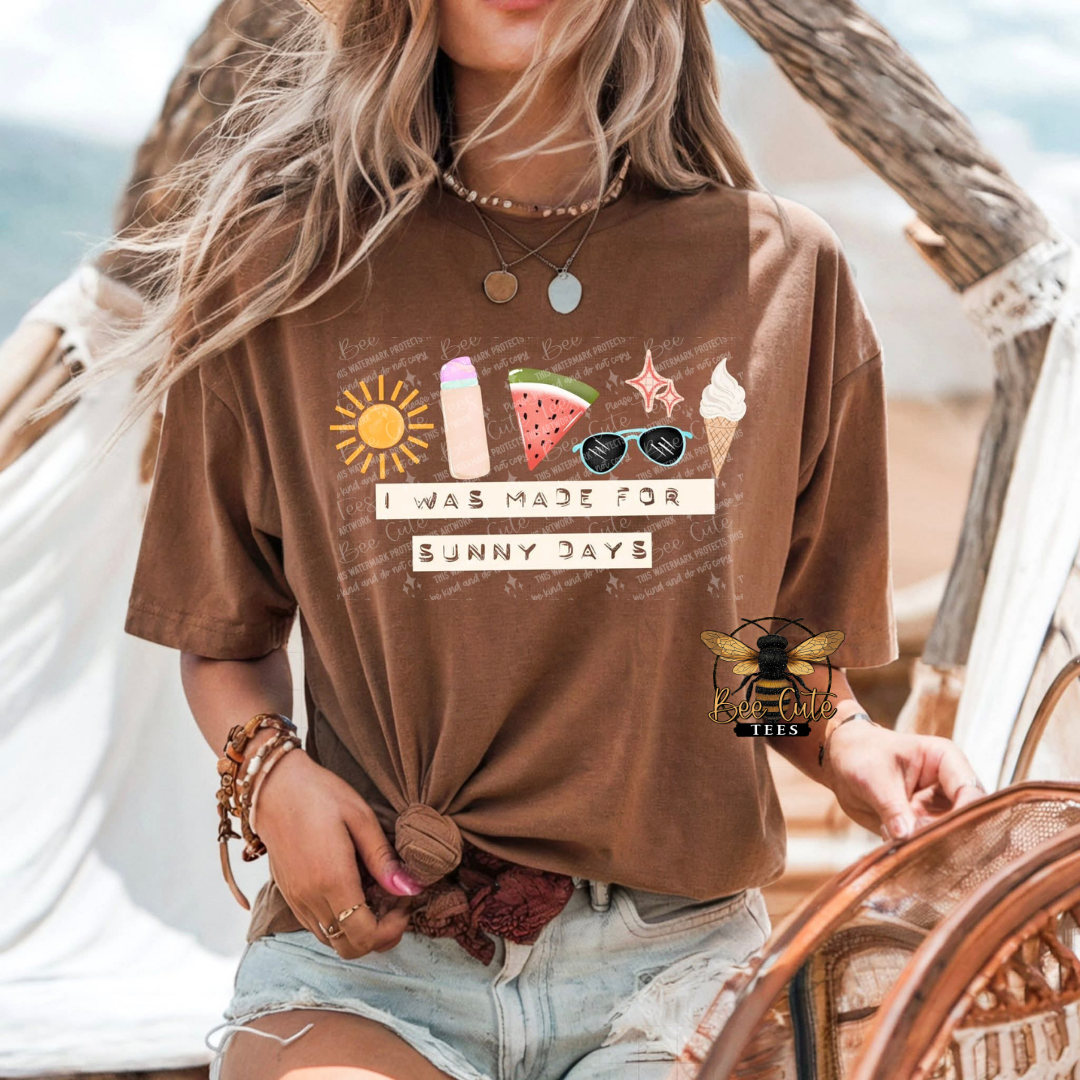 Person wearing a brown t-shirt with beach-themed graphics and text, sitting on a wooden chair.