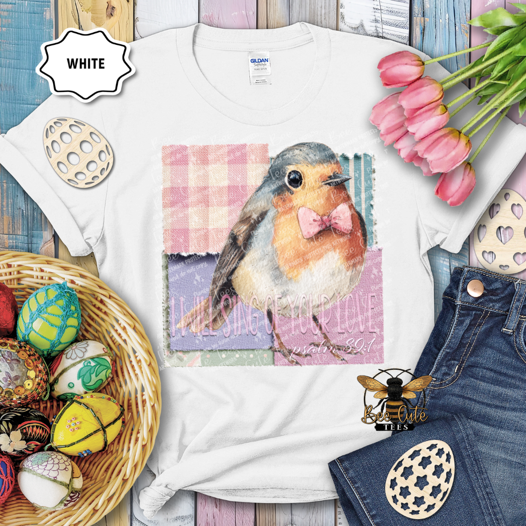 White t-shirt with a bird graphic and text, surrounded by Easter decorations on a wooden surface.