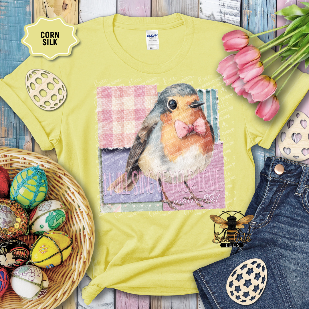 Yellow t-shirt with a robin design and Easter decorations on a wooden surface.