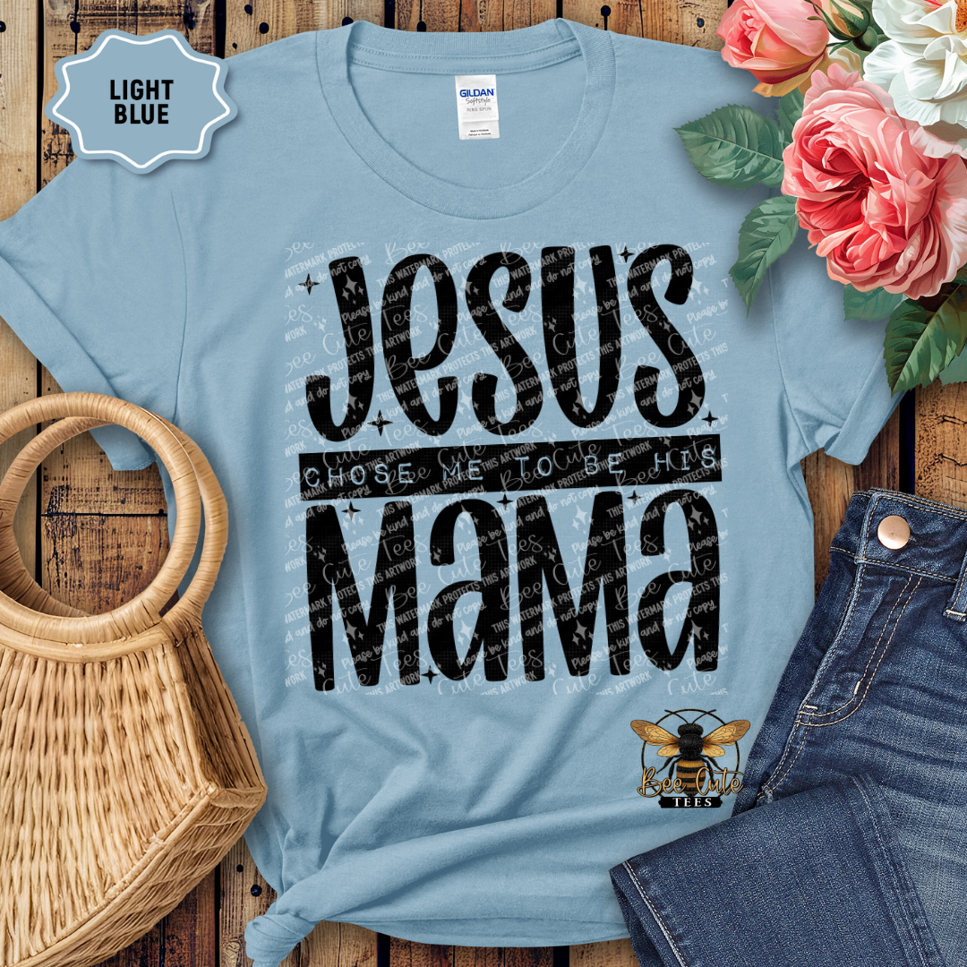 Light blue t-shirt with 'Jesus Chose Me to be His Mama' text, surrounded by flowers and denim jeans on a wooden surface.