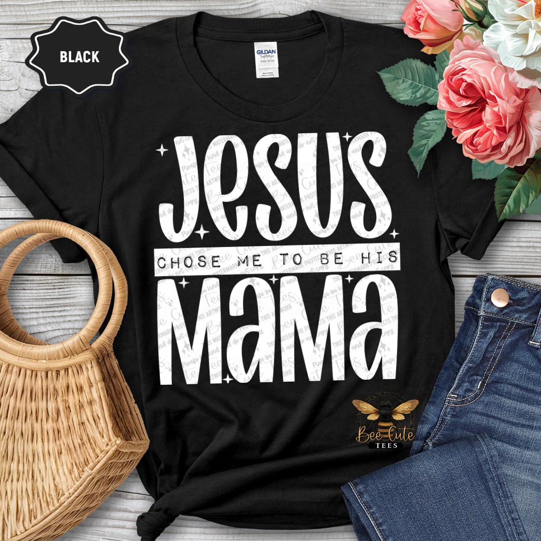 Black t-shirt with 'Jesus chose me to be his mama' text, surrounded by flowers and jeans on a wooden surface.