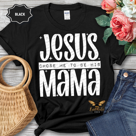 Black t-shirt with 'Jesus chose me to be his mama' text, surrounded by flowers and jeans on a wooden surface.
