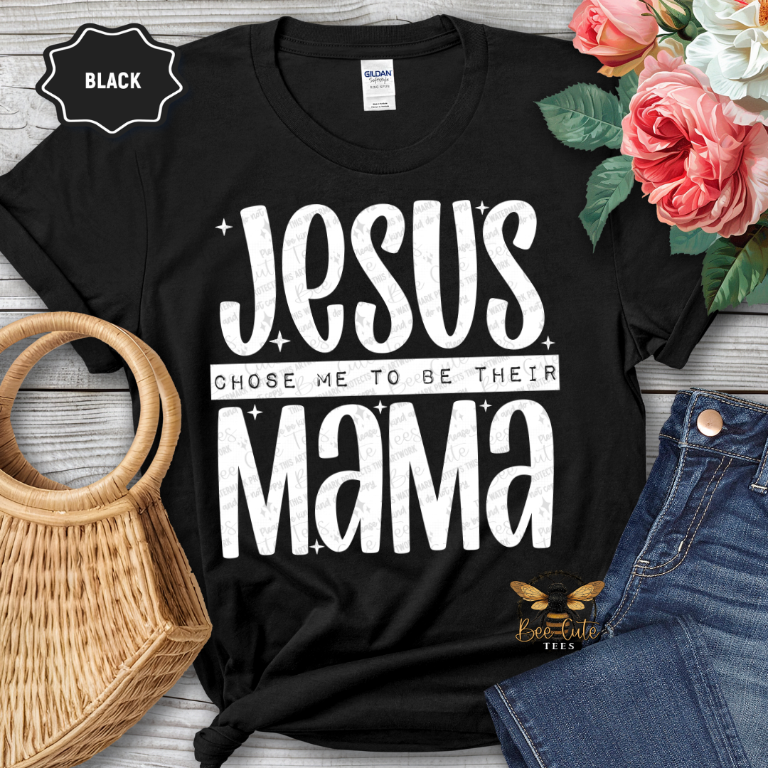 Black t-shirt with 'Jesus chose me to be their mama' text, surrounded by flowers and jeans on a wooden surface.