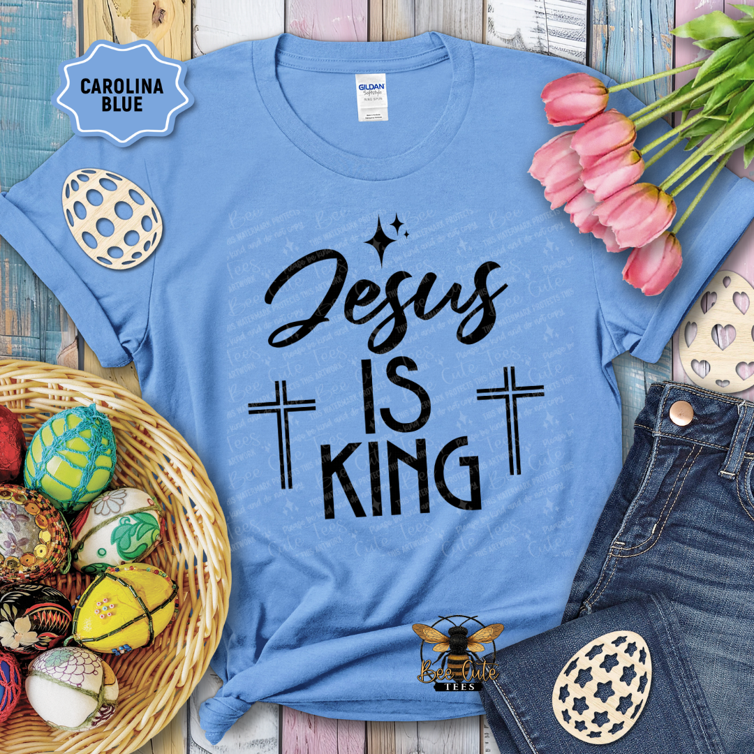 Blue t-shirt with 'Jesus is King' text, surrounded by Easter decorations on a wooden surface.