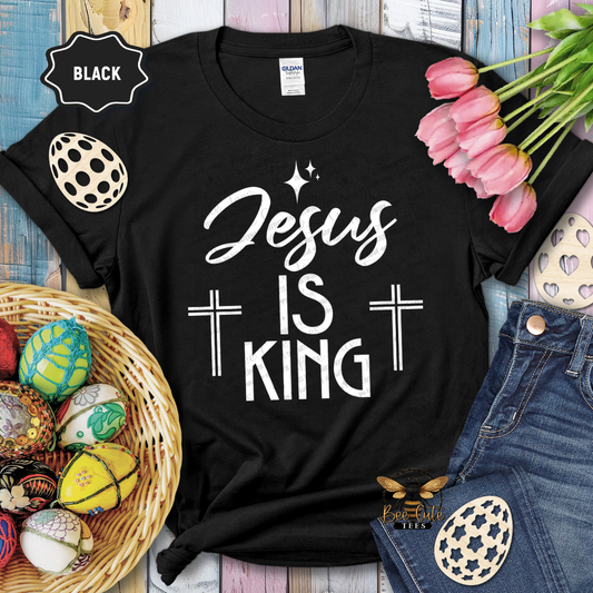 Black t-shirt with 'Jesus is King' text, surrounded by Easter decorations on a wooden surface.
