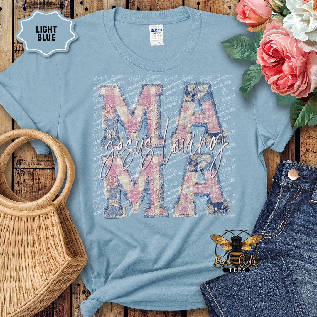 Light blue t-shirt with 'Jesus loving MAMA' design on a wooden surface with flowers and denim jeans.