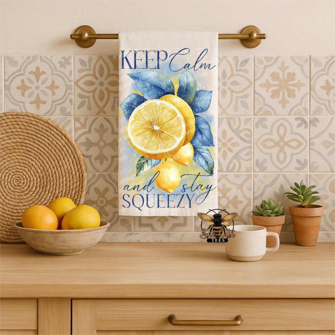 Kitchen towel with lemon design and text hanging on a towel rack, with lemons and a cup on the counter.