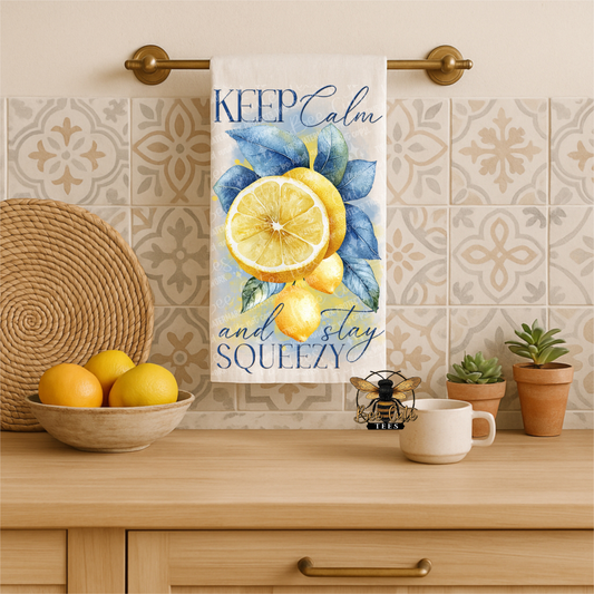 Kitchen towel with lemon design and text hanging on a towel rack, with lemons and a cup on the counter.
