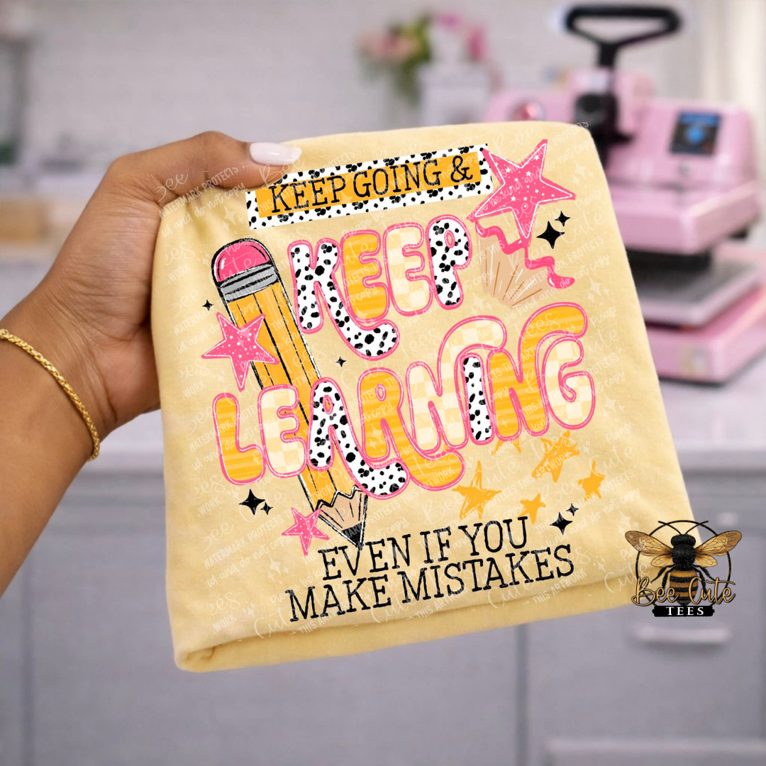Hand holding a yellow t-shirt with motivational quote and graphics in a craft room setting