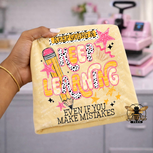 Hand holding a yellow t-shirt with motivational quote and graphics in a craft room setting