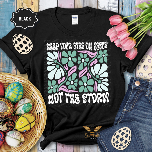 Black t-shirt with floral design and text, surrounded by Easter decorations on a wooden surface.
