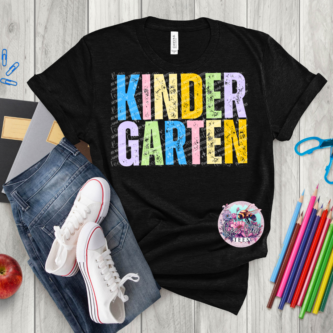 Black t-shirt with 'KINDER GARTEN' in colorful letters on a wooden surface with jeans, sneakers, and school supplies.