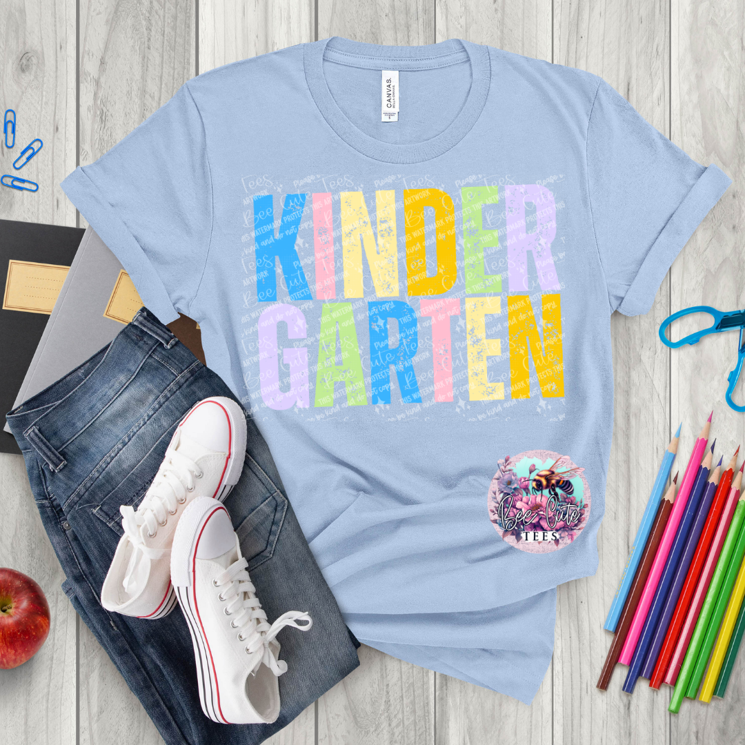 Light blue t-shirt with 'KINDER GARTEN' print on a wooden surface with jeans, sneakers, and school supplies.