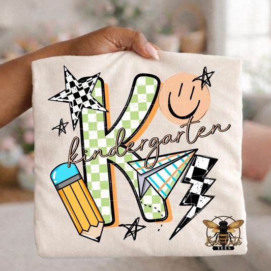 Folded white-colored unisex T-shirt held up by a hand, featuring a colorful "kindergarten" graphic. The design includes green checkered number four, bold black lettering, peach script, a pencil, paper airplane, smiley face, lightning bolt, stars, and playful doodles. A fun, retro-inspired back-to-school design perfect for fourth grade teachers and students.
