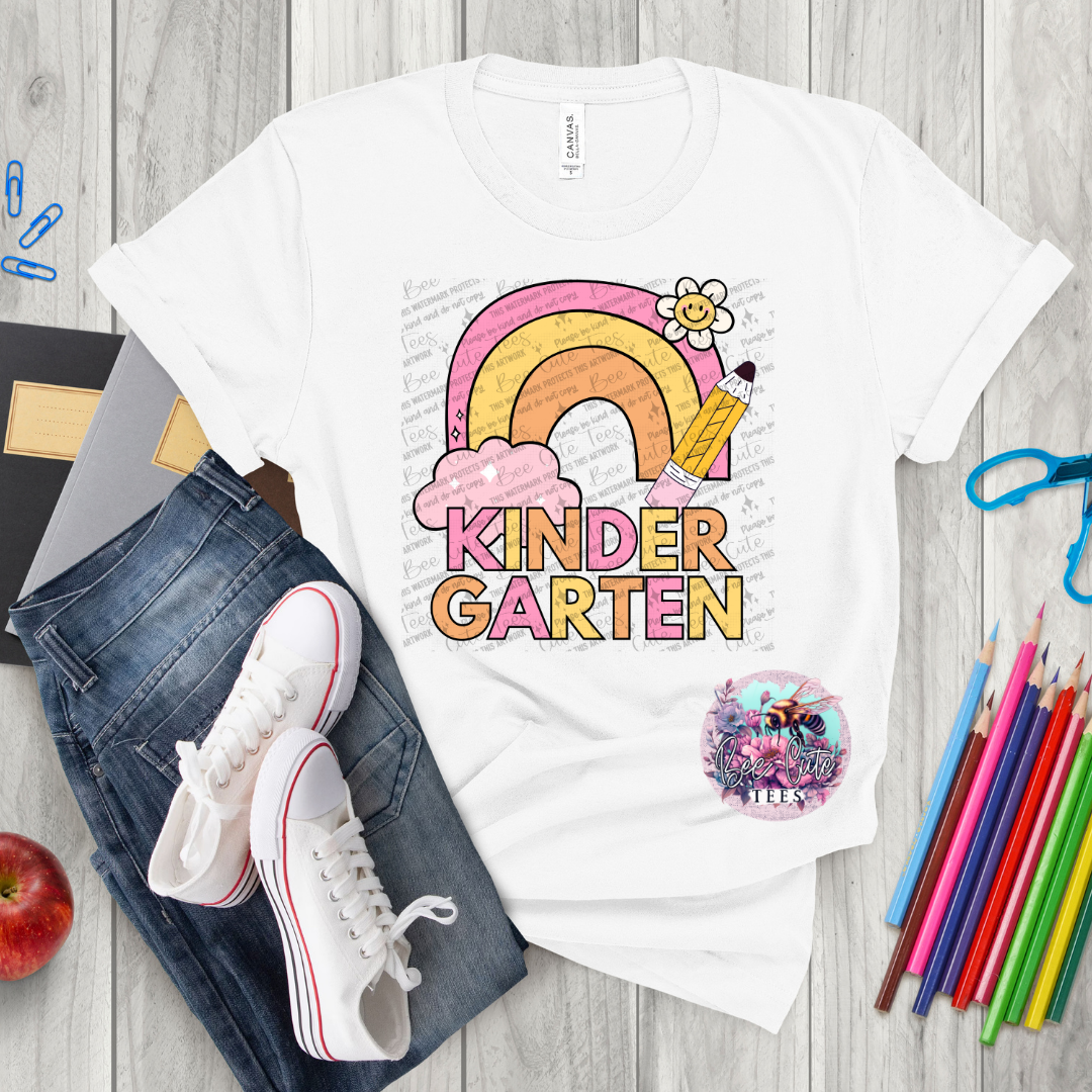 White t-shirt with 'Kinder Garten' design on a wooden surface with jeans, sneakers, and school supplies.