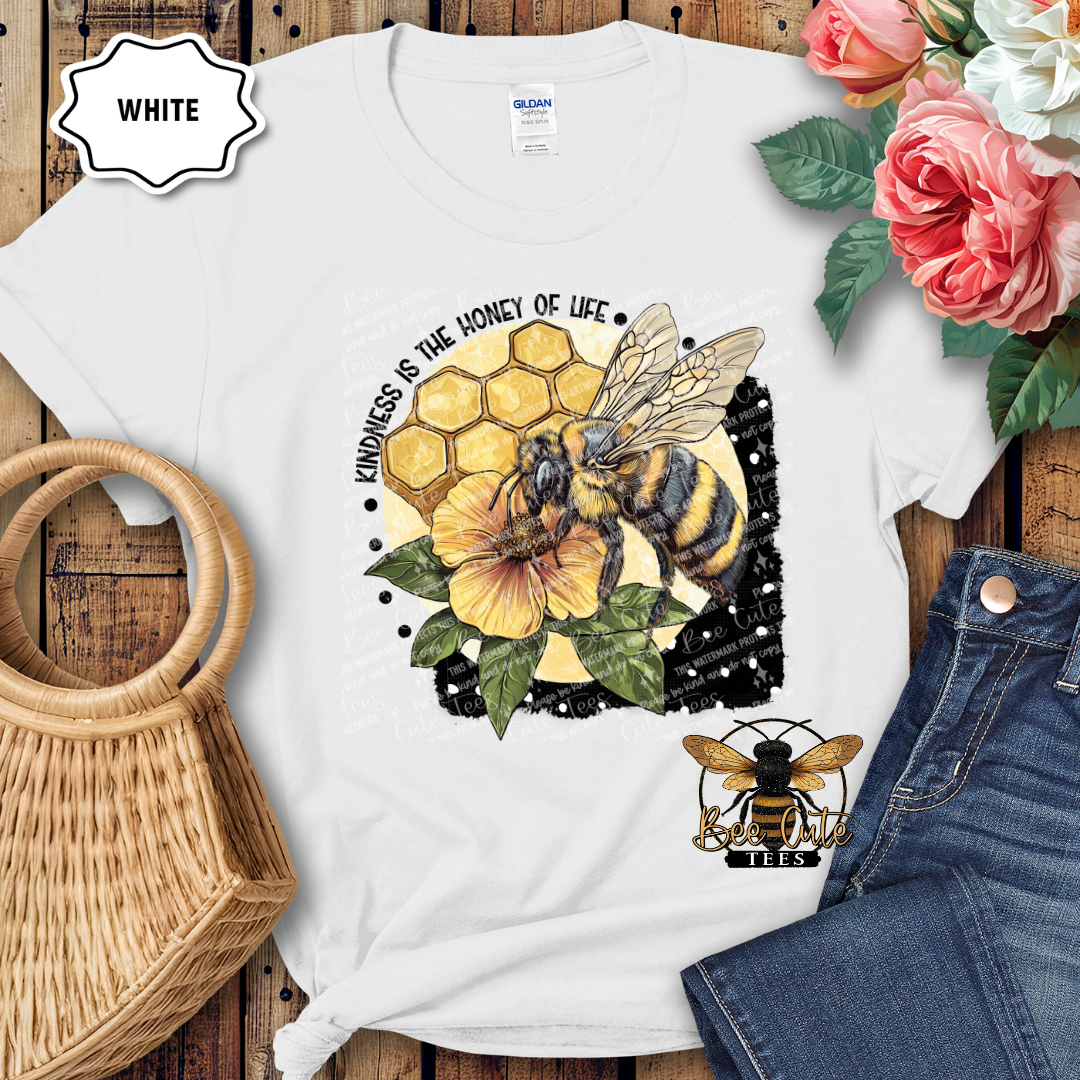 White t-shirt with bee and honeycomb design on a wooden surface with flowers and jeans.