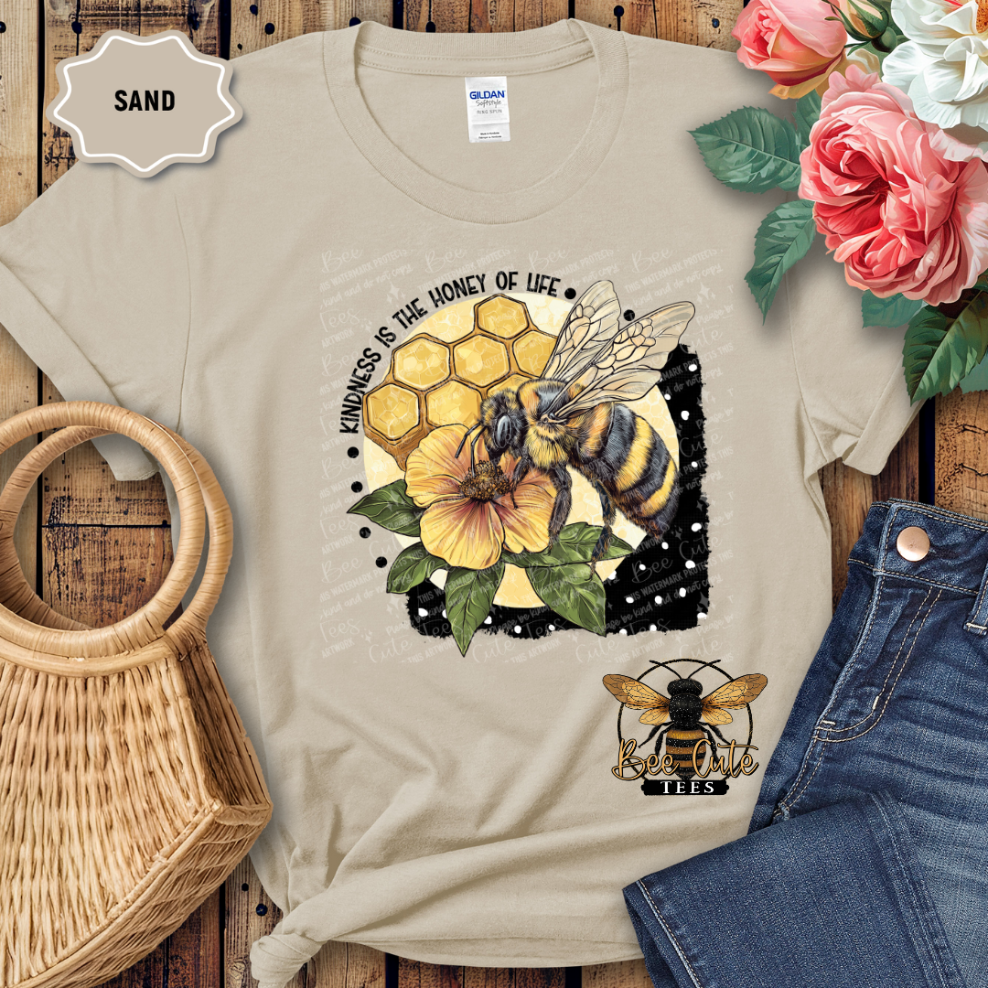Beige t-shirt with bee and honeycomb design on a wooden surface with flowers and jeans.