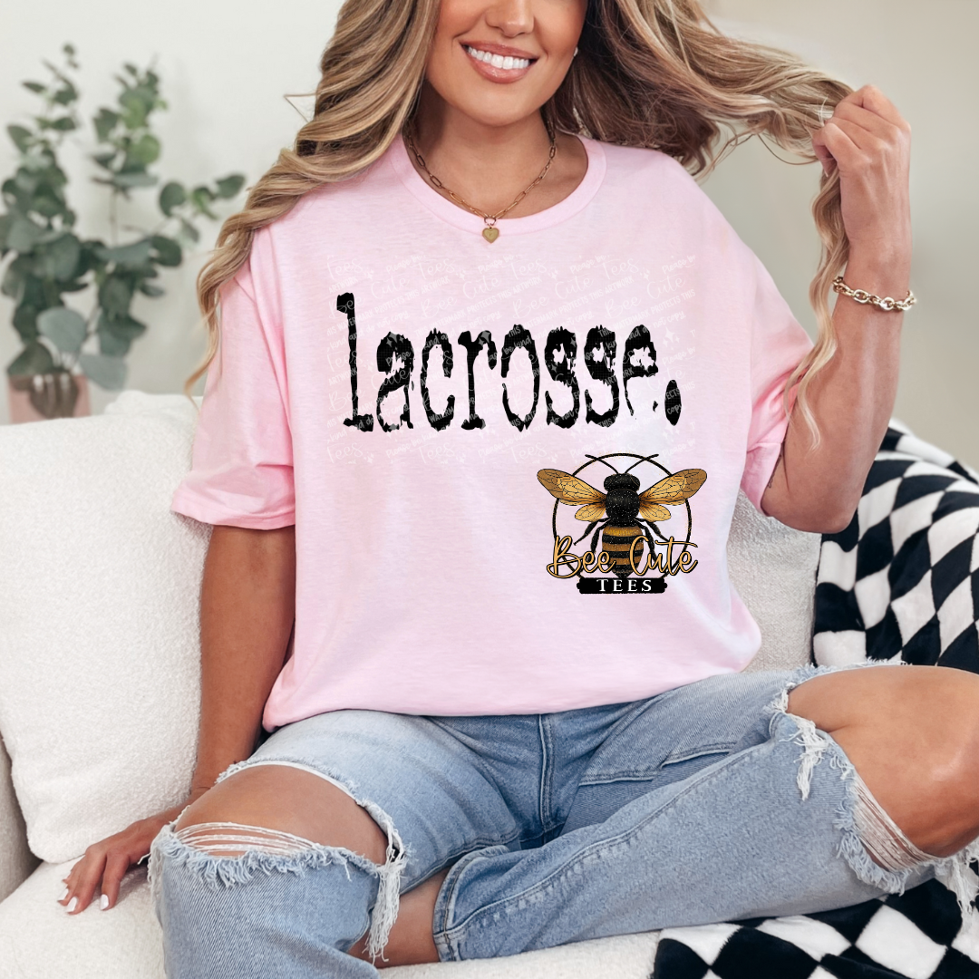 Woman wearing a pink t-shirt with 'lacrosse' and a bee logo, sitting on a couch.