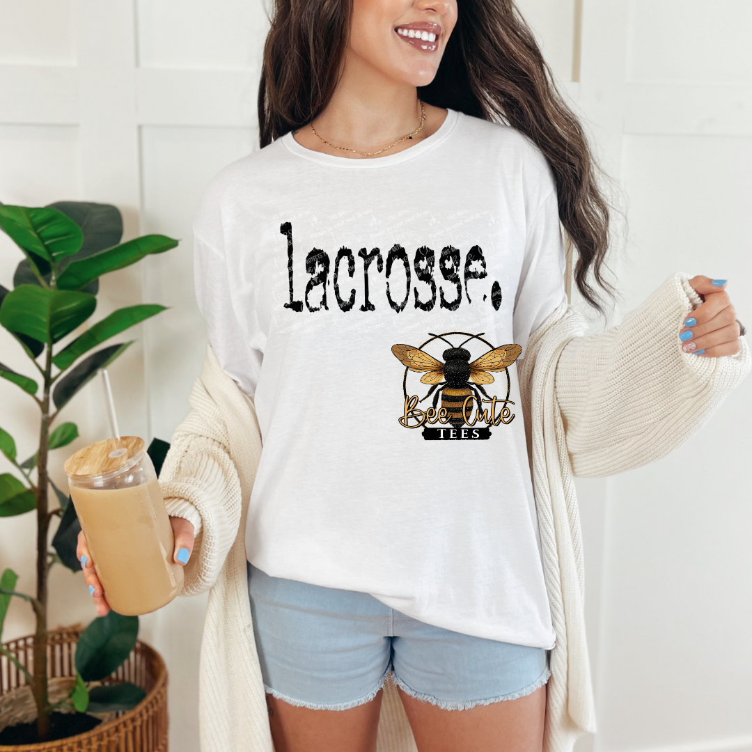 woman wearing a white t-shirt with the text 'lacrosse' standing while holding a drink.