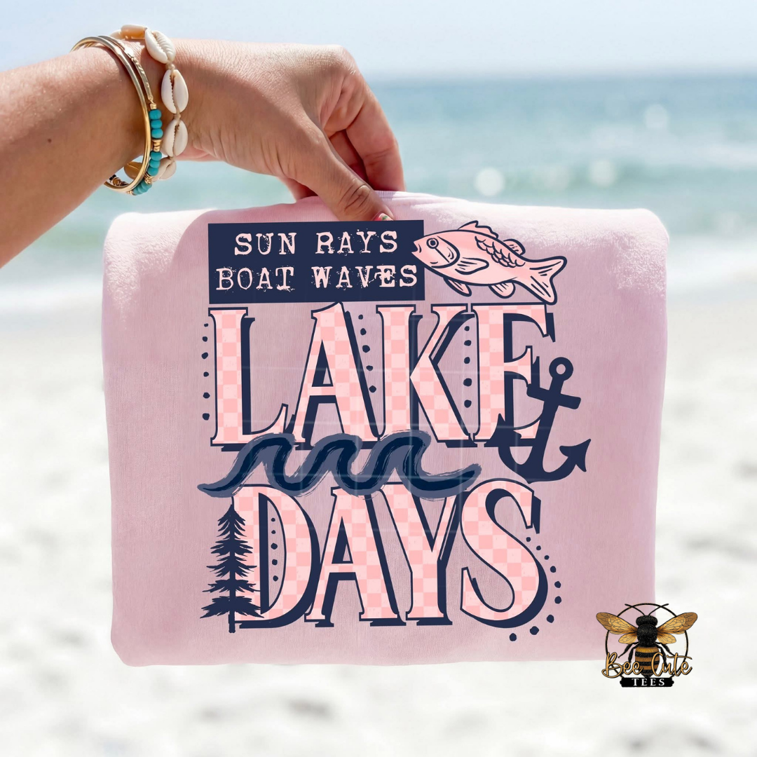 Pink t-shirt with 'Lake Days' text held by a hand against a beach background